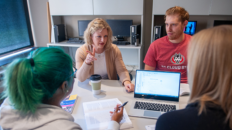 Professor seated around table with three graduate students