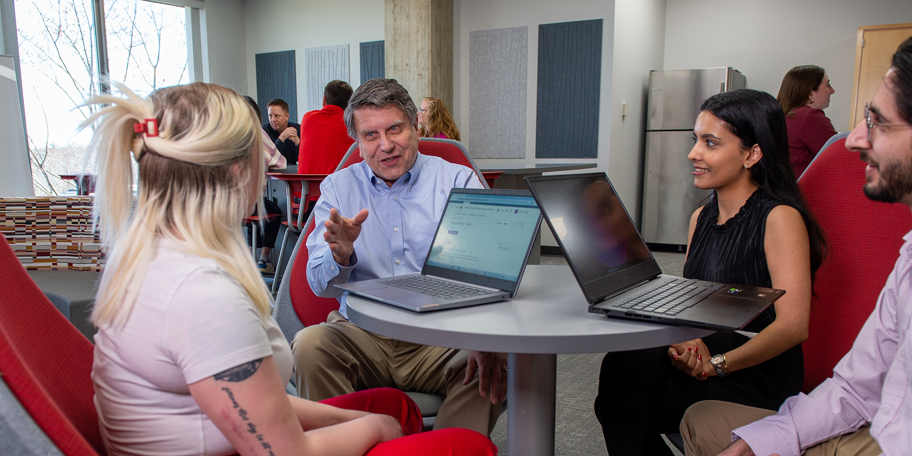 Professor seated and talking with three students