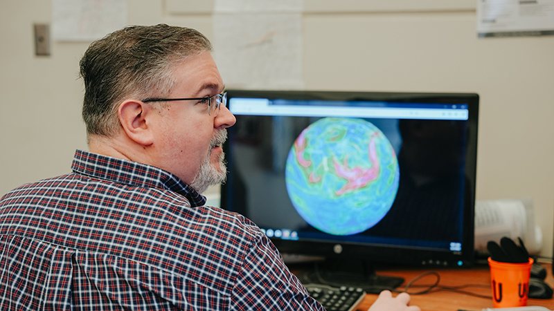 Prof. Alan Srock seated at computer with globe on it