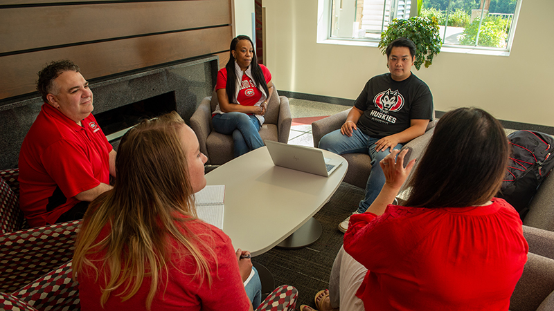 Small group of faculty and students seated and talking by fireplace