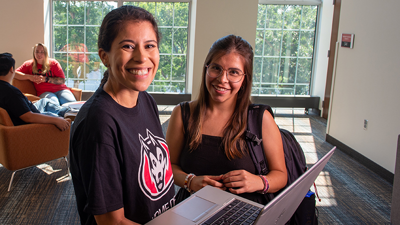 Two students standing and smiling while looking at laptop