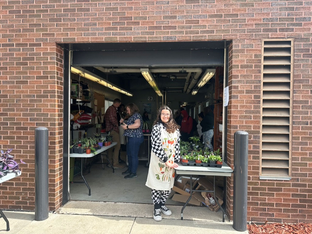 a student presenting a collection of small plants near the greenhouse