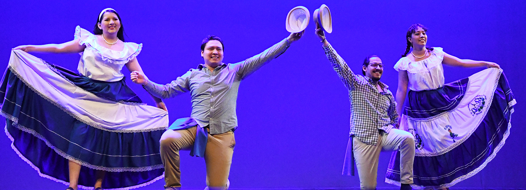 Four students dancing on stage in traditional attire