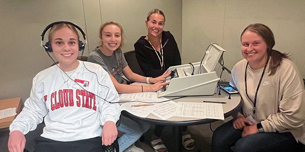 Four students seated at table working with audiology equipment