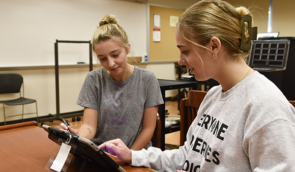 Two young women seated at table using touch screen device