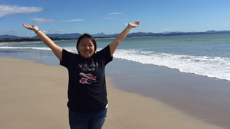 Student on beach with arms up in excitement