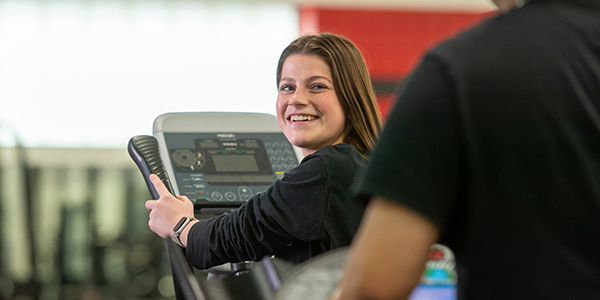 Student on treadmill looking over her shoulder and smiling at the person behind her