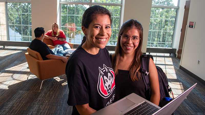 Two students smiling together with laptop