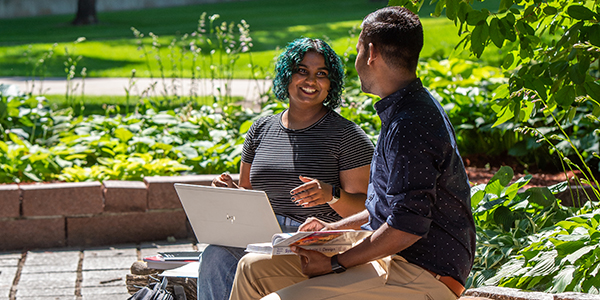 Two students with laptops outdoors talking to one another