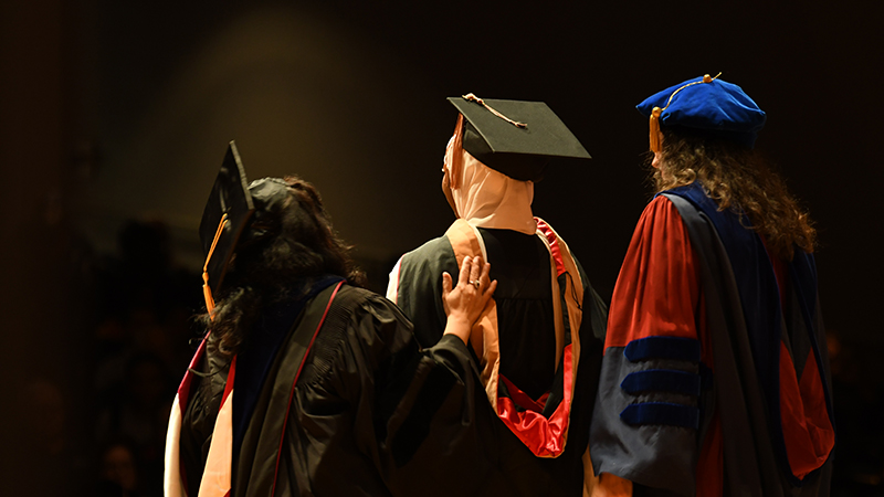 View from behind of a faculty putting graduate hood on student