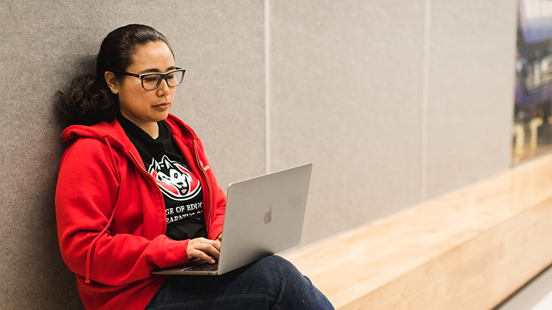 Student in red hoddie seated on floor working on laptop