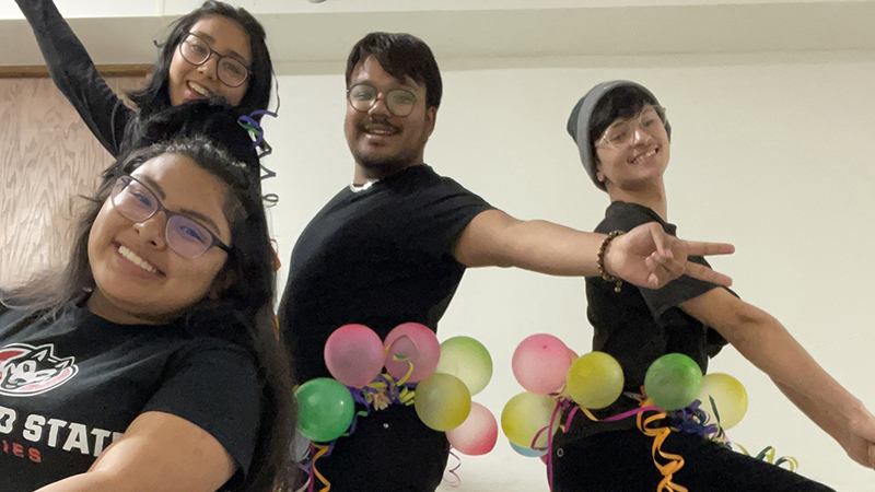 Four students with balloons smiling at camera