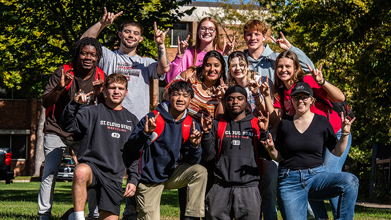 Large group of students gathered doing the sign of the Husky with their hands