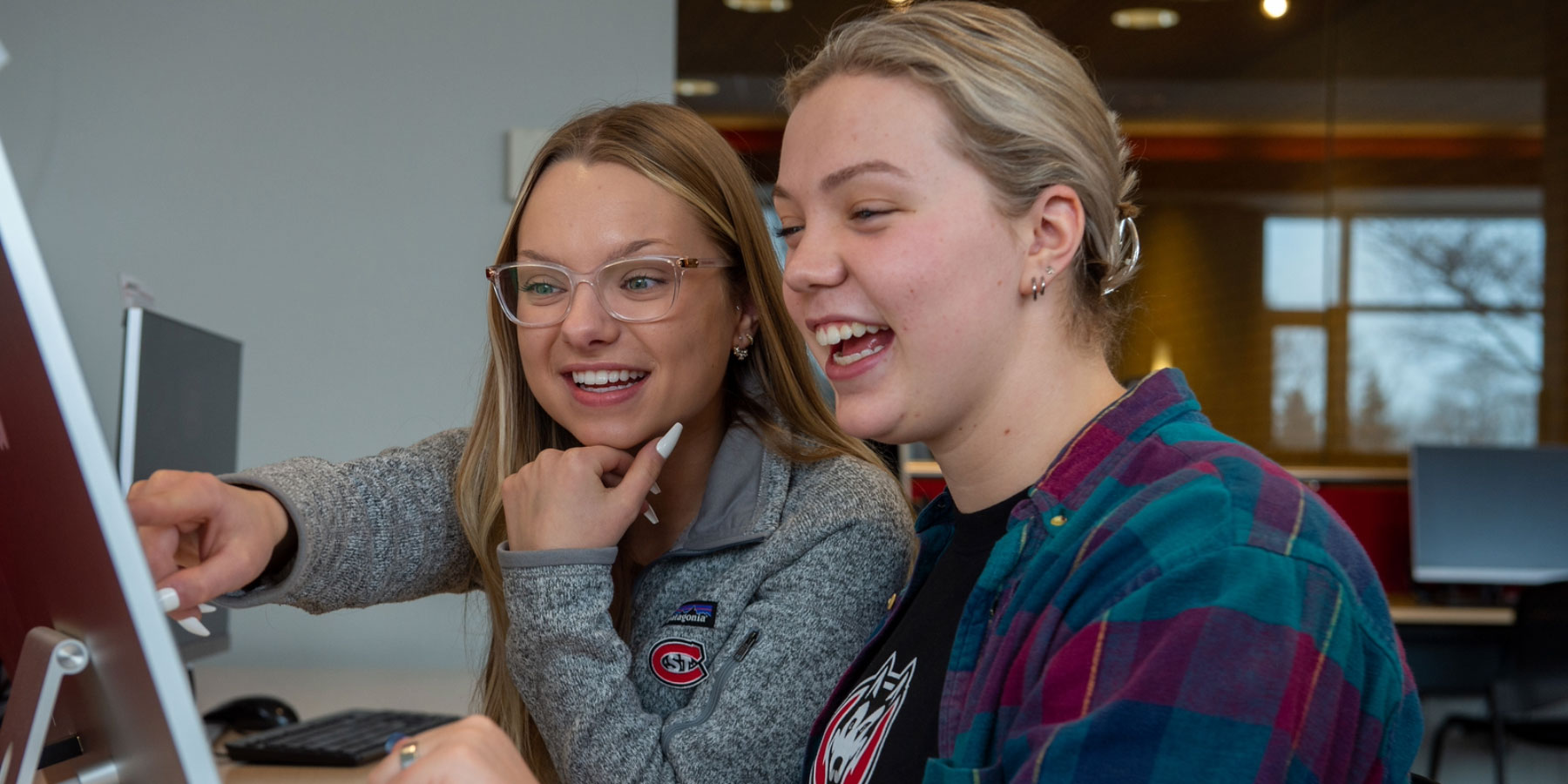 two students wearing clothes with SCSU logo looking at computer smiling with one person pointing at screen  