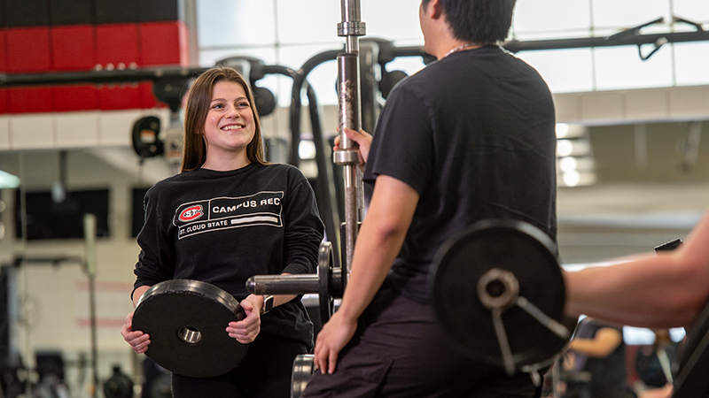 Student holding a large weight and talking to another