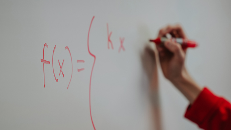 Close-up of hand writing math problem out on white board