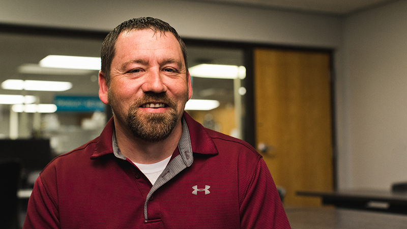 Man in maroon pullover lightly smiling at camera