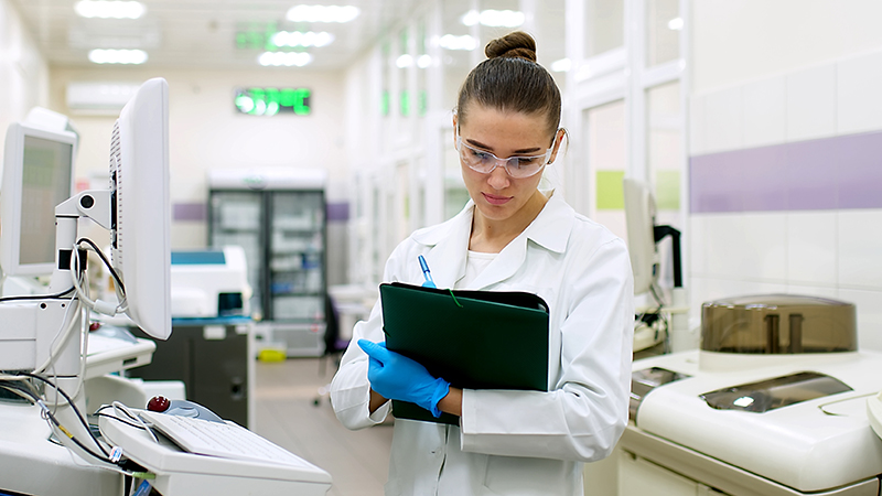 Woman standing in lab setting writing on clipboard