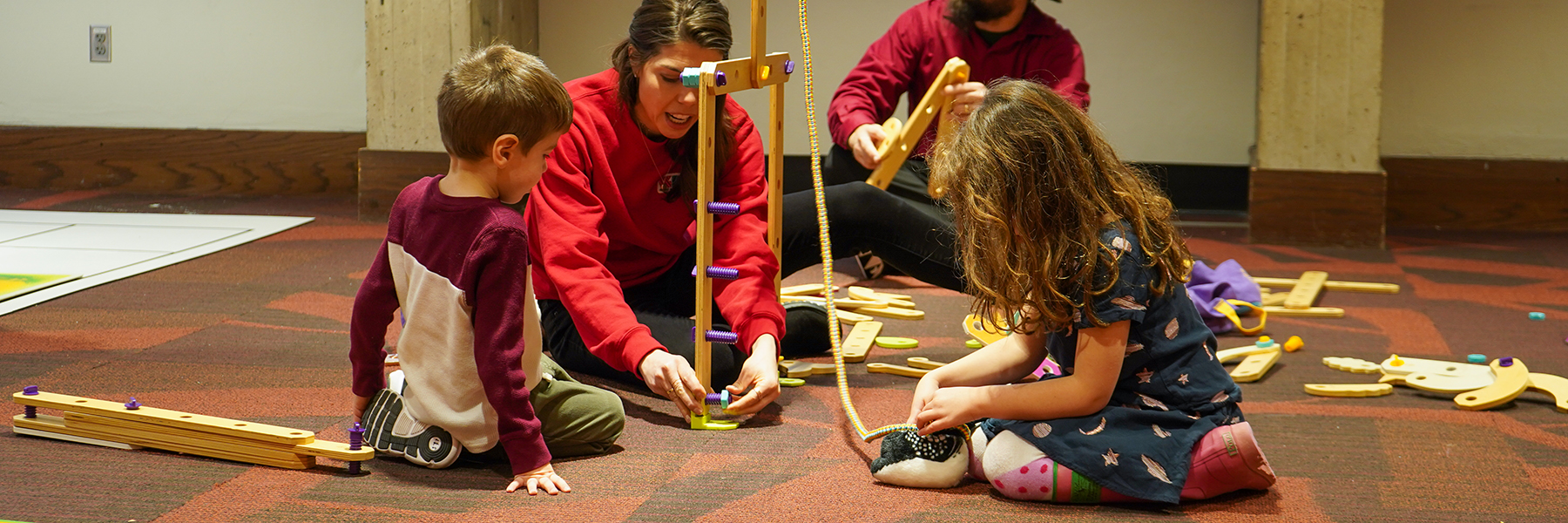 Two children playing on carpeted floor with adult woman