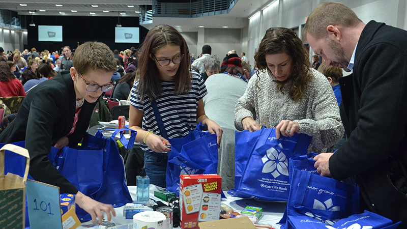 Four people stuffing bags with essential need items