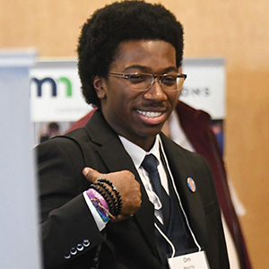 Student dressed in suit standing and smiling among others in a room