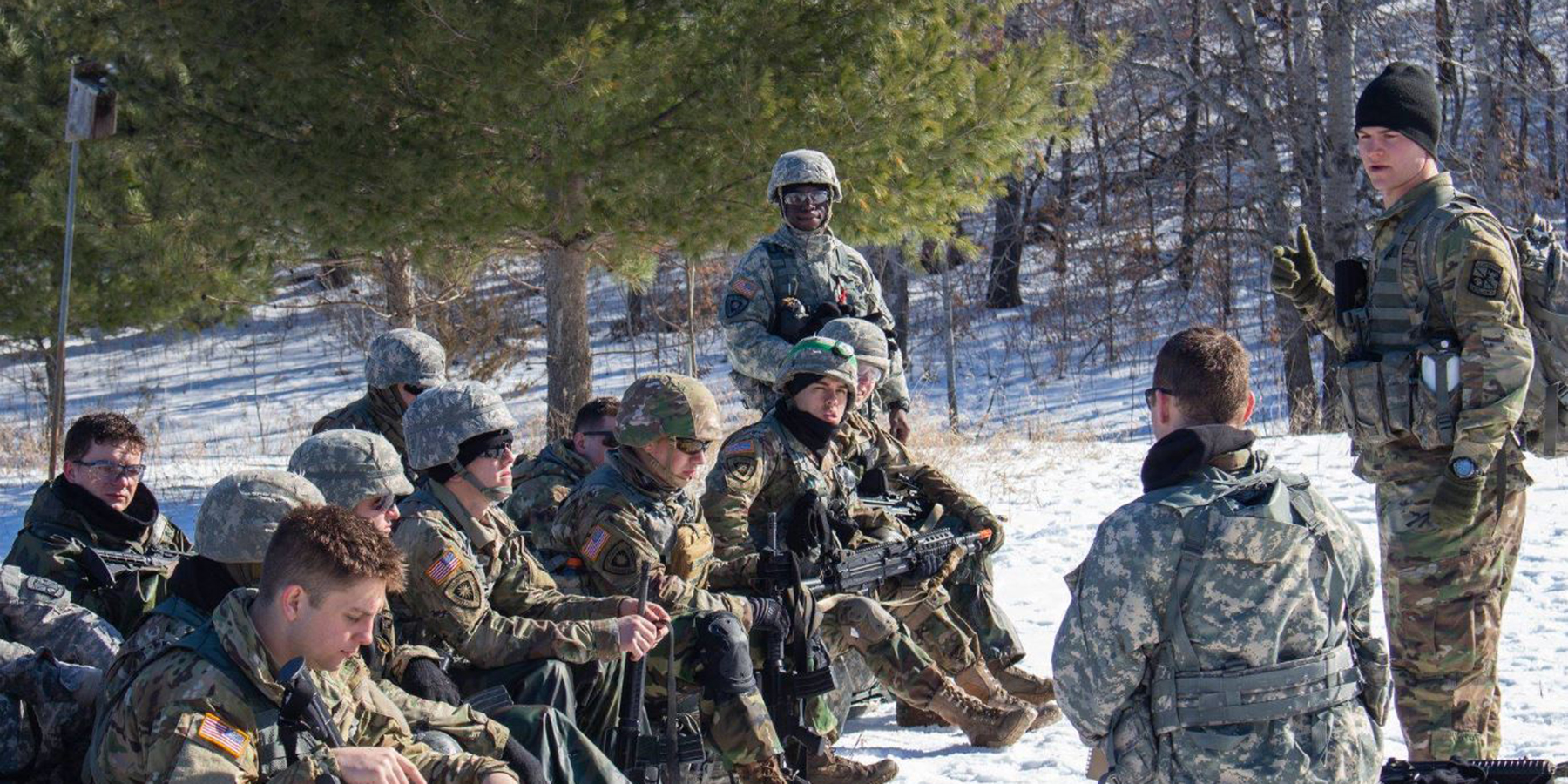 Cadet talking to fellow cadets seated outdoors in snow