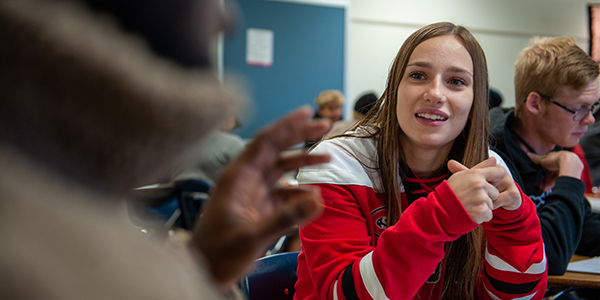 Female student in hockey jersey speaking with other student in class