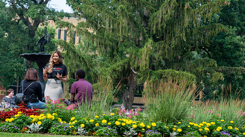 Three students gathered in outdoor park with flowers