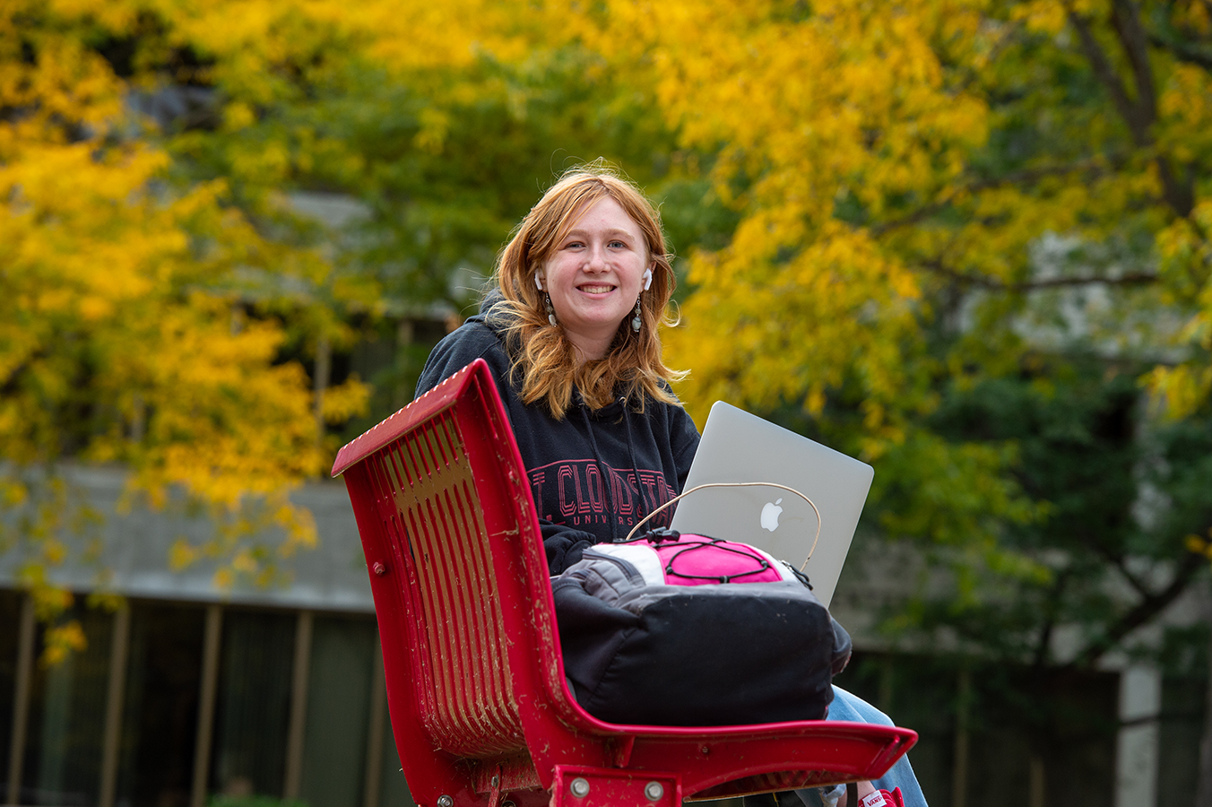 Student with laptop sitting on red bench outside