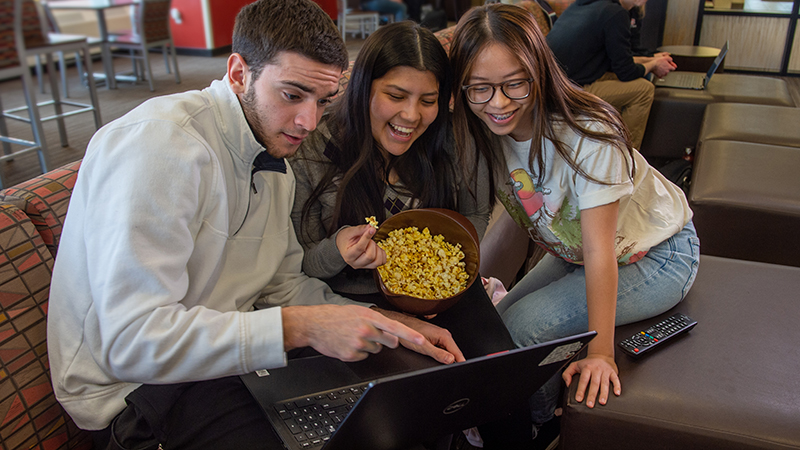 Three students gathered around laptop and eating popcorn