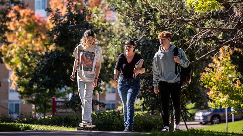 Three students walking to class from residence hall in background