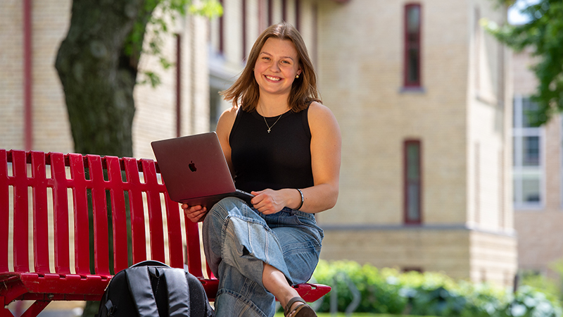 Young female student seated on red campus bench with laptop