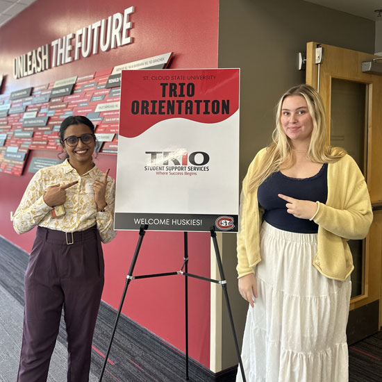 two female students standing by a sign that reads "TRIO Orientation"