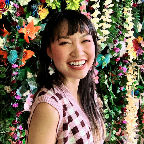  A woman smiles for a photo in front of a wall of flowers