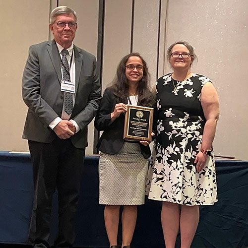 Three people smile on stage with an award